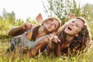 A pair of young women smiling and laughing in a field with straight, white teeth.